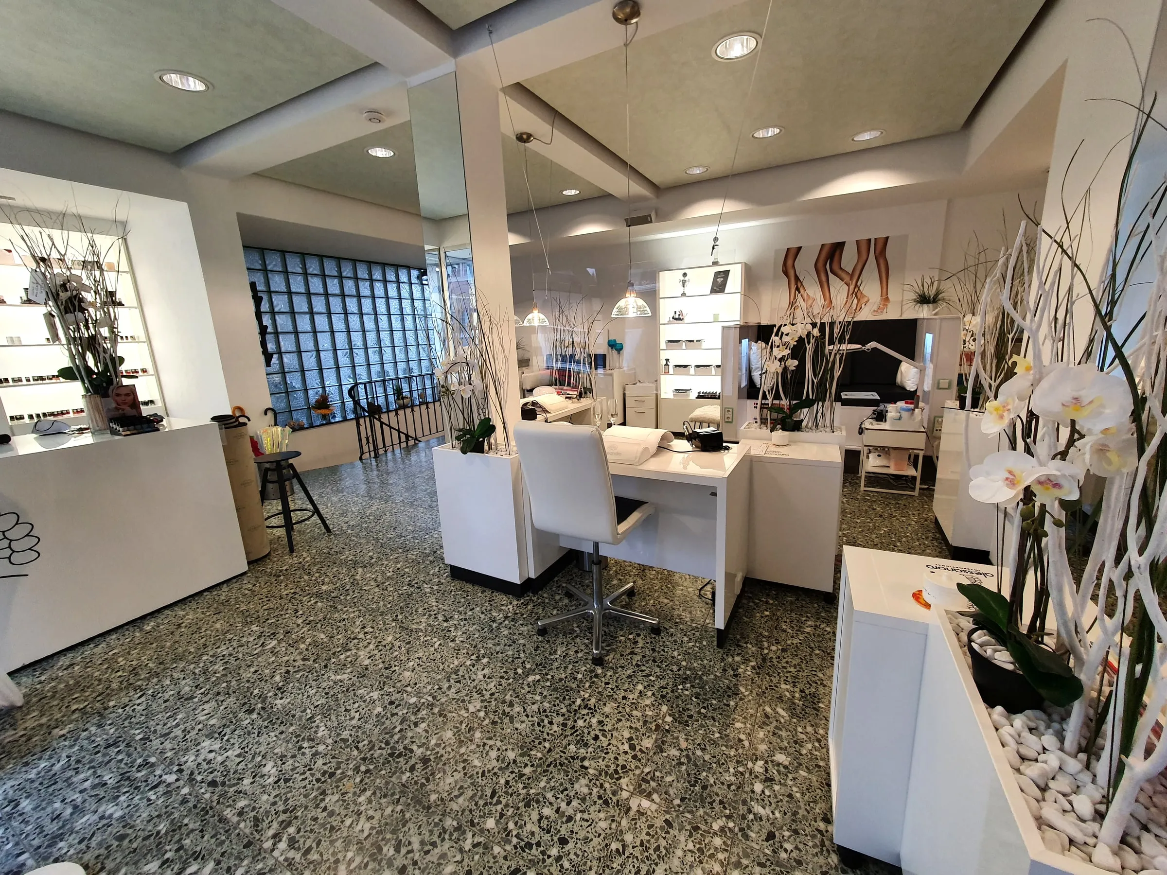 Das Studio von innen: weiße Nageltische, Terrazzo-Boden, Orchideen und Glasbausteinwand